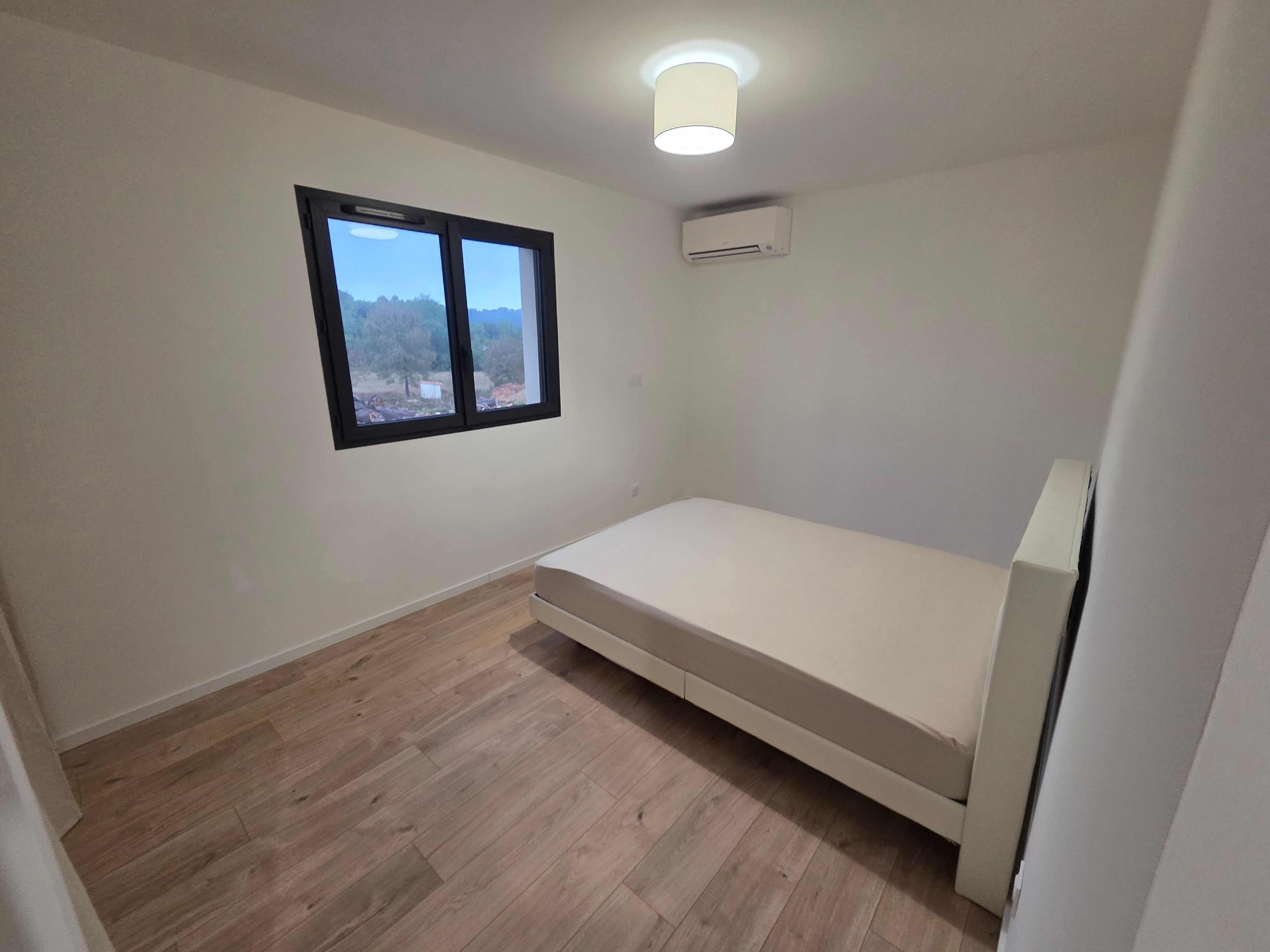 Ein kleines Zimmer mit einem Einzelbett, einem Fenster mit Ausblick und einer Klimaanlage.
