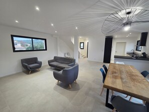 A modern interior with a dining area, sofas, a TV, and a kitchen.