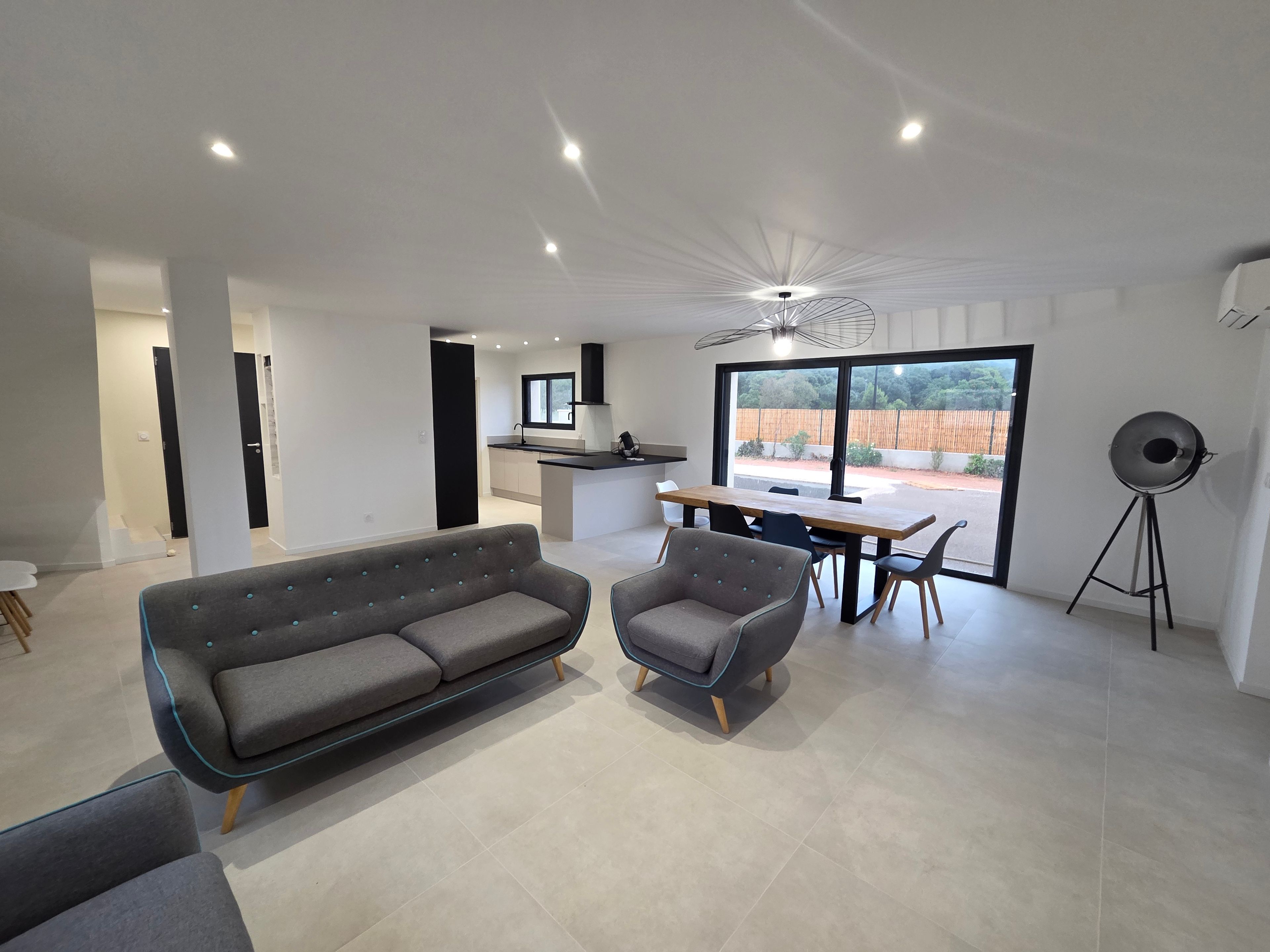 Ein modernes Wohnzimmer mit einer Couch und Sesseln, ein Essbereich mit Tisch und Stühlen sowie eine Küche im Hintergrund.