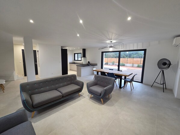 A modern living room with a sofa and chairs, a dining area with a table and chairs, and a kitchen in the background. - Holiday Home 'La Villa De Jade' with Mountain View, Wi-Fi and Air Conditioning (Murles)