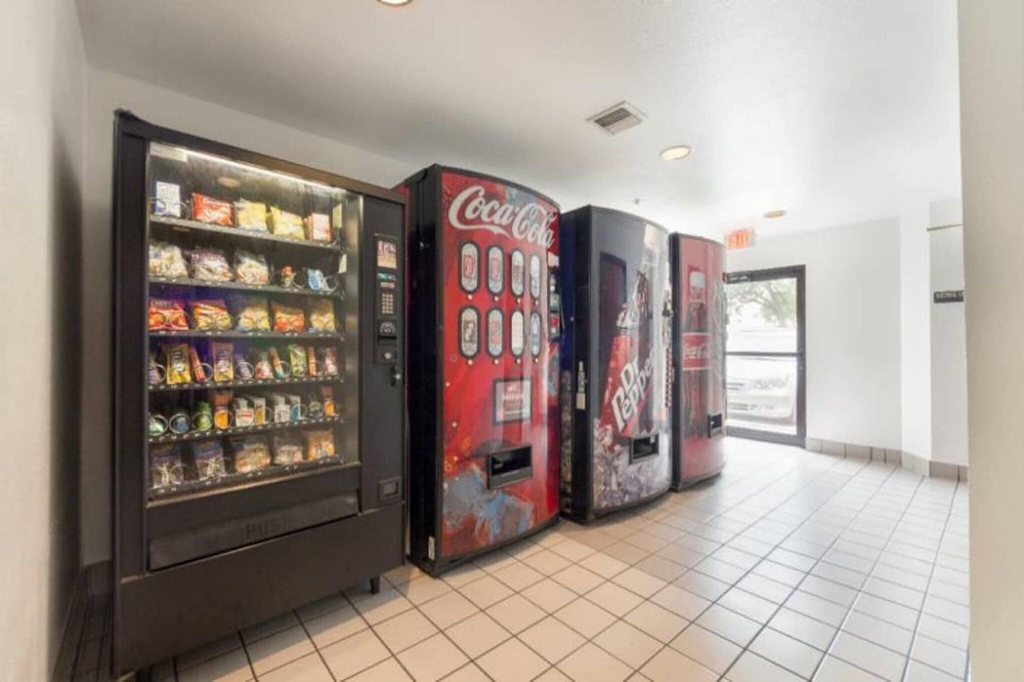 A row of vending machines with snacks and beverages, including Coca-Cola and Diet Pepsi, in a clean, tiled hallway.