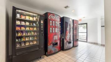 A row of vending machines with snacks and beverages, including Coca-Cola and Diet Pepsi, in a clean, tiled hallway.