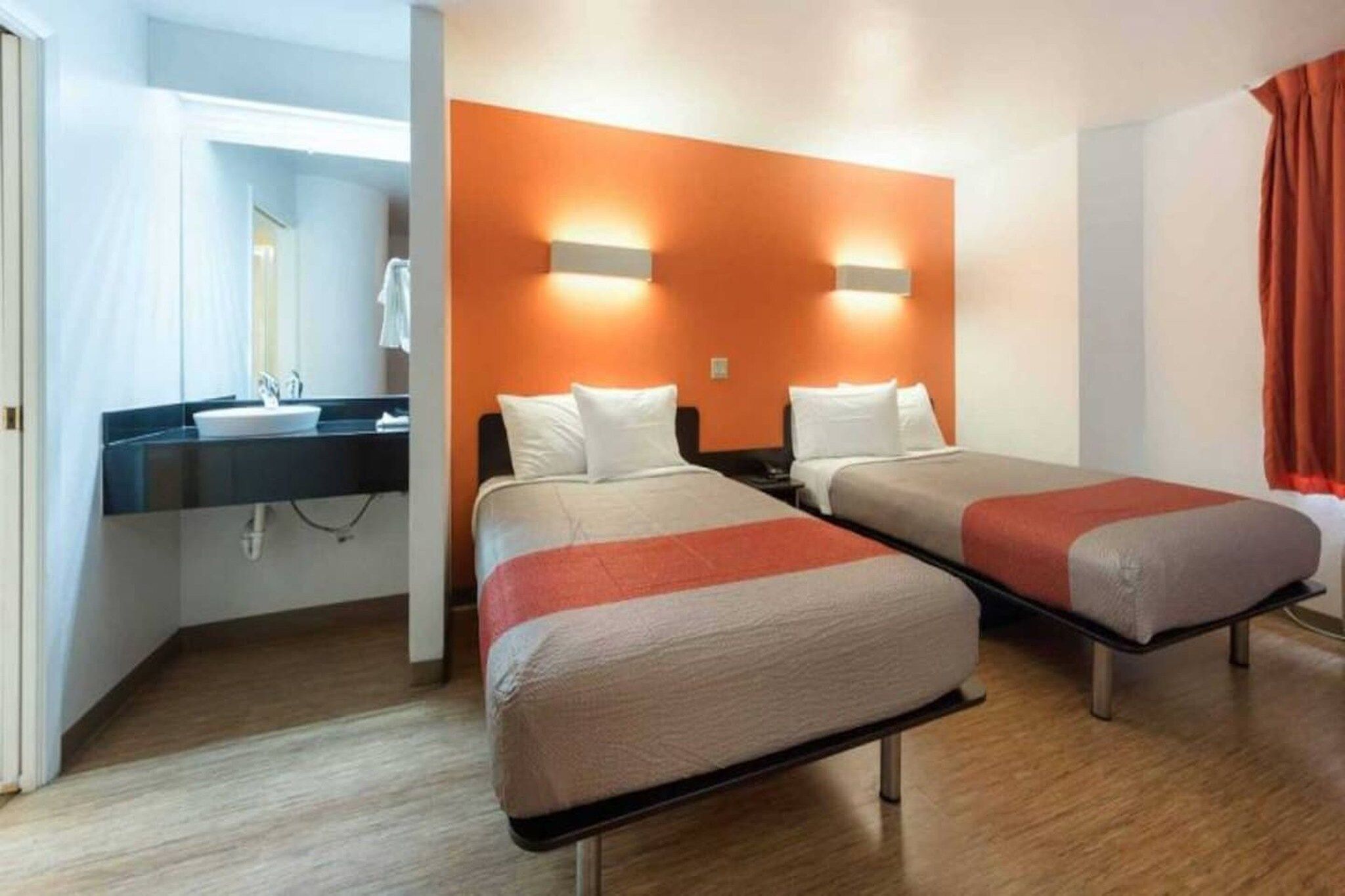 A hotel room with two beds, a bathroom with a sink, and a mirror.