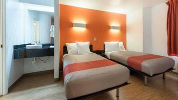 A hotel room with two beds, a bathroom with a sink, and a mirror.