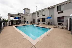 A rectangular pool with a no diving sign, surrounded by a concrete deck, a fence, and a building with multiple windows and a small tower.