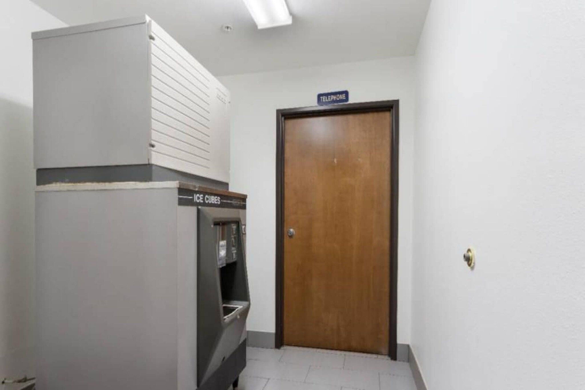 A room with a refrigerator, an ice dispenser, and a wooden door with a 'telephone' sign above it.
