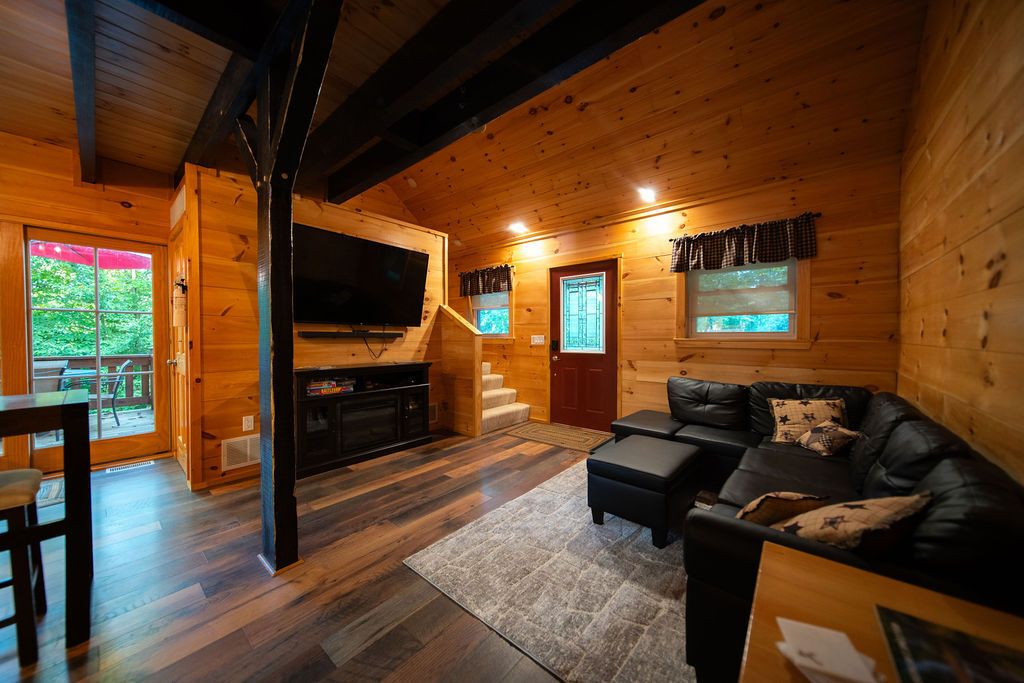 Interior de una cabaña de madera con chimenea, un sofá de cuero negro y un comedor.