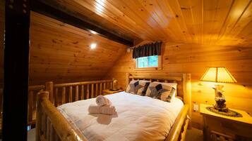 Ein Schlafzimmer einer Holzhütte mit einem Bett, einem Nachttisch, einer Lampe und einem Fenster mit Vorhängen.