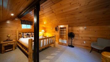A wooden cabin room with a bed, bedside table, lamp, and a chair.