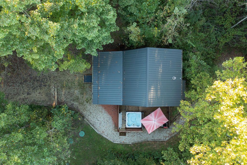 Eine kleine, dunkel gefärbte Holzhütte mit Whirlpool und einem rosafarbenen Sonnenschirm in einem bewaldeten Gebiet.