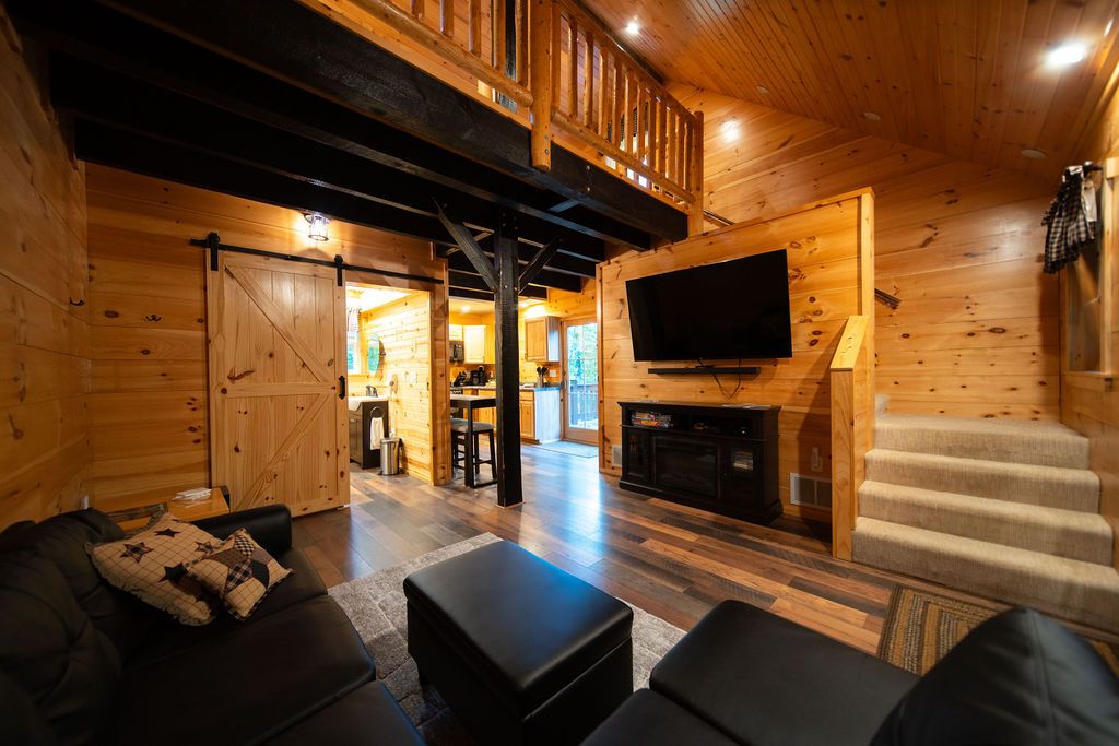A log cabin interior with a living room, a fireplace, a television, and a staircase.