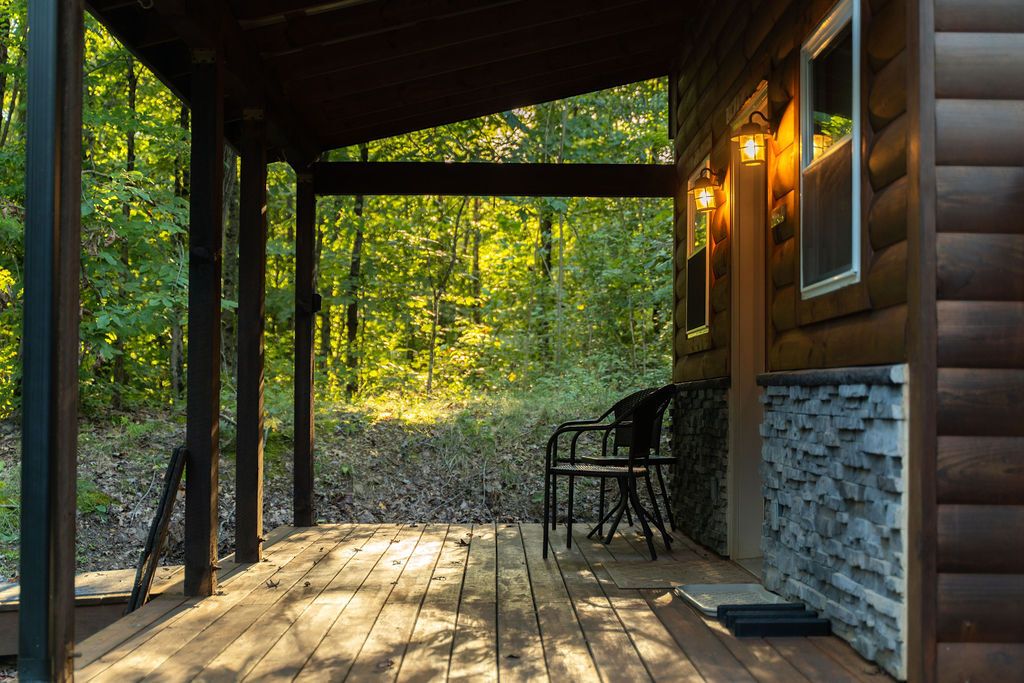 A wooden deck with a covered area, stone wall, and two chairs.