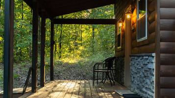 A wooden deck with a covered area, stone wall, and two chairs.
