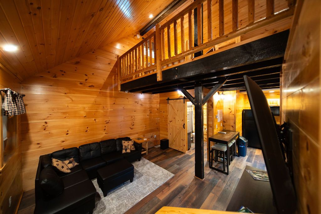 A wooden interior with a loft area, a black leather sofa, and a dining table.