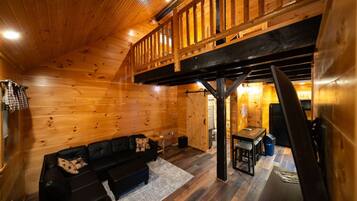 A wooden interior with a loft area, a black leather sofa, and a dining table.
