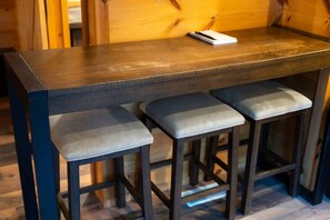 A bar stool with a cushioned seat and a dark wooden table. - Turkey Trail | Hocking Hills, Hot Tub, Secluded (Logan)