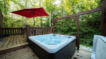 Ein Whirlpool auf einer Holzterrasse mit einem roten Sonnenschirm.