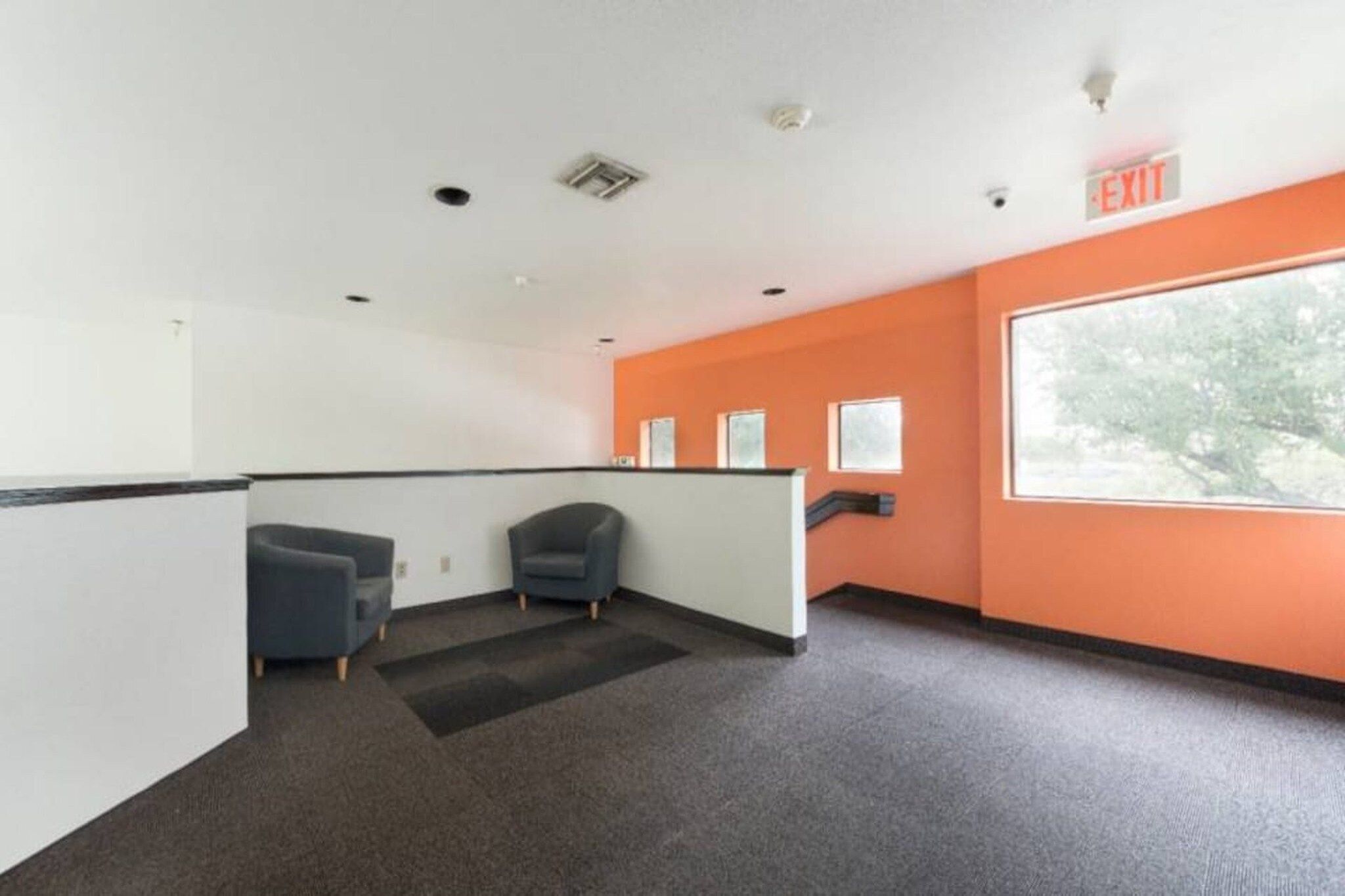 A modern office space with cubicles, a large window, and an exit sign.