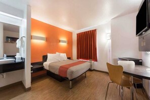 A hotel room with a bed, a desk, a chair, a television, and a bathroom.