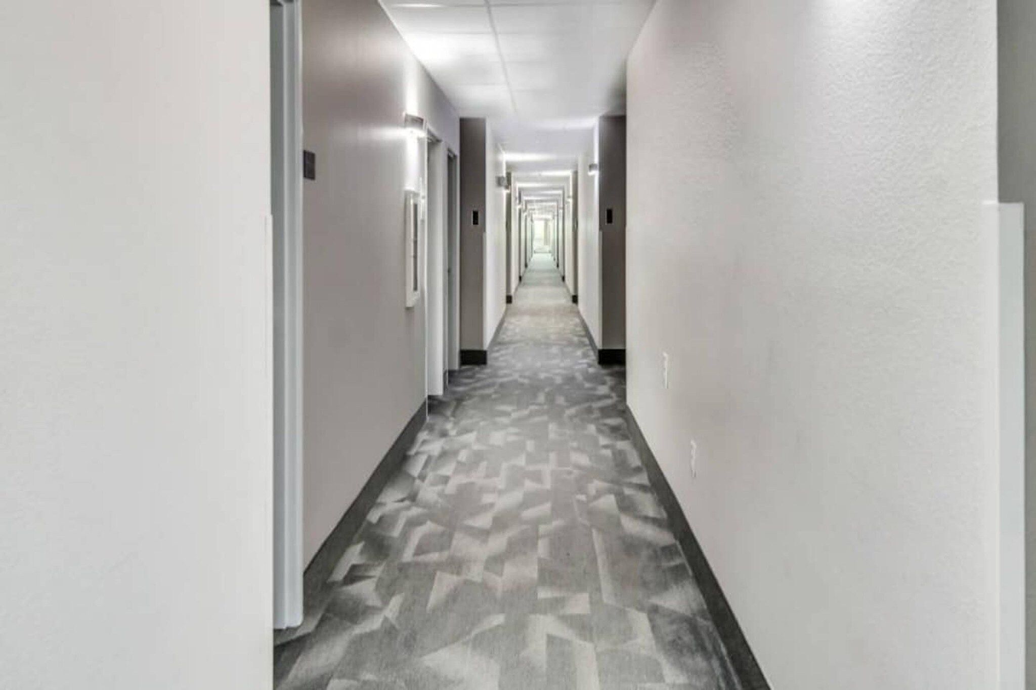 A long, straight hallway with doors on both sides, leading to rooms. The floor has a patterned tile design.