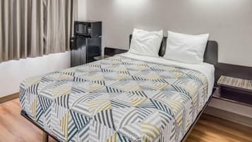 A hotel room with a bed, a nightstand, a microwave, and a window with curtains.