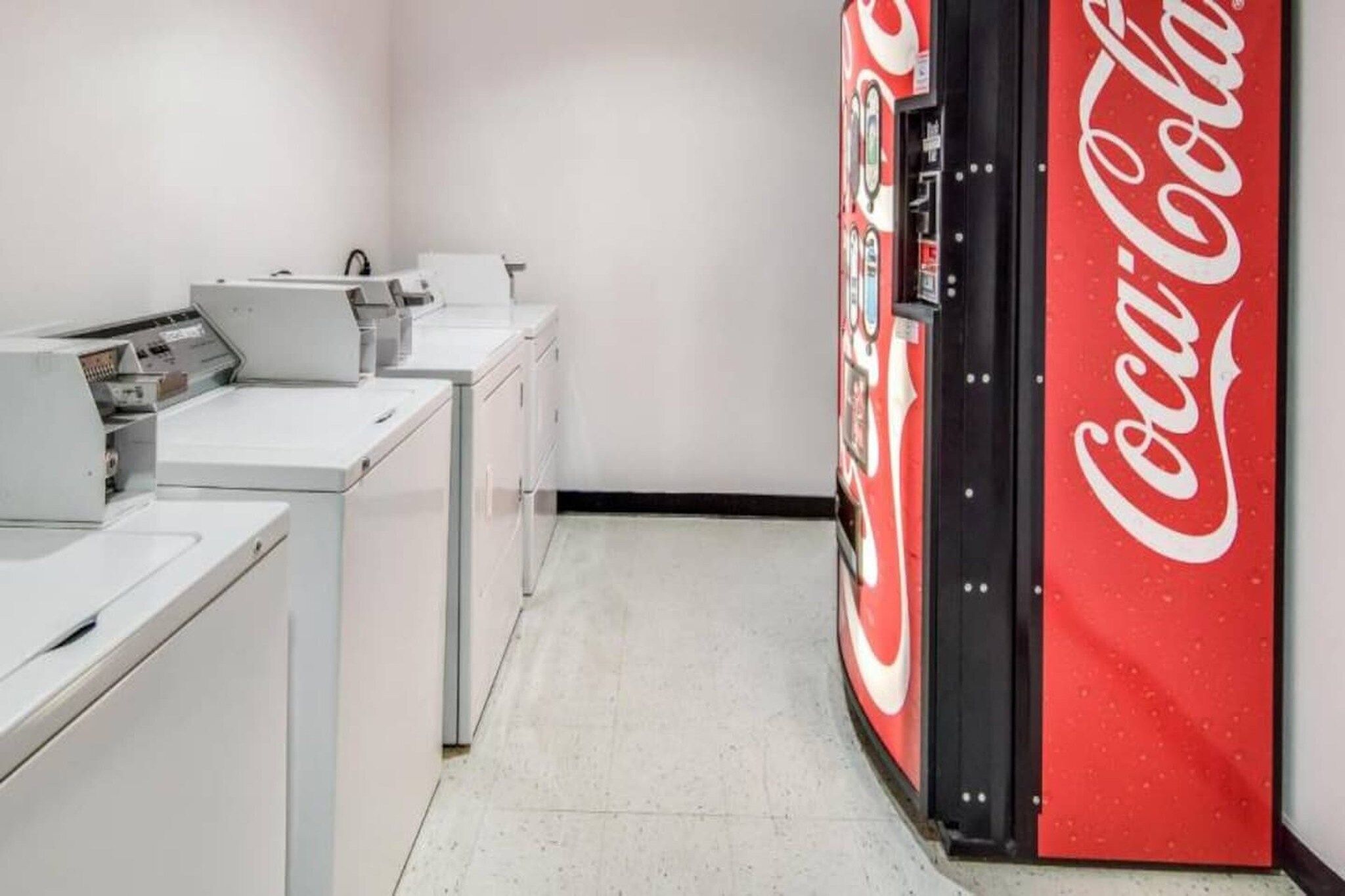 A laundromat with rows of washing machines and dryers, and a Coca-Cola vending machine.
