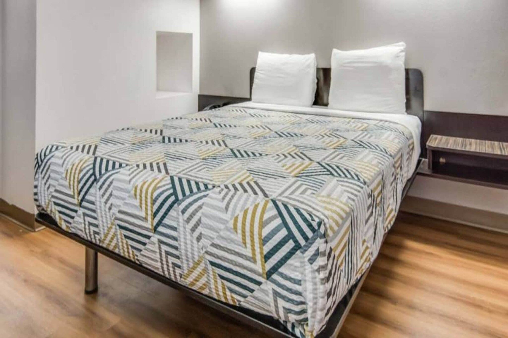 A bed with a patterned bedspread, a headboard, and a bedside table with a lamp.