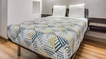 A bed with a patterned bedspread, a headboard, and a bedside table with a lamp.