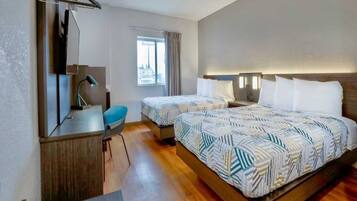 A hotel room with two beds, a desk, a chair, and a window.