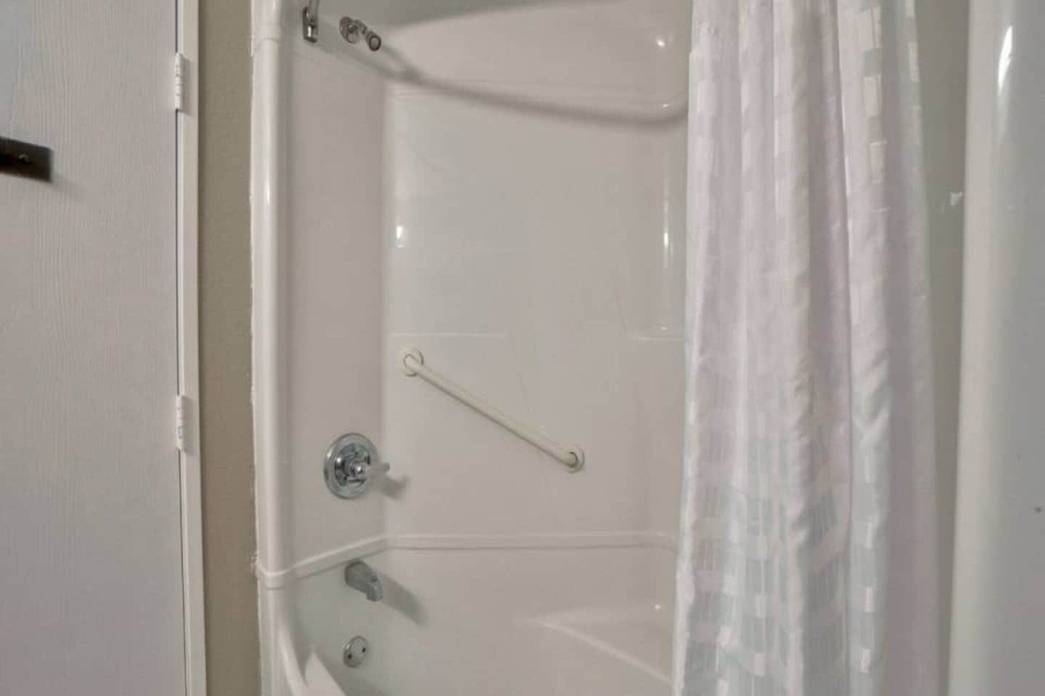 A white bathtub with a shower curtain, a grab bar, and a faucet.