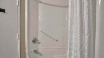 A white bathtub with a shower curtain, a grab bar, and a faucet.