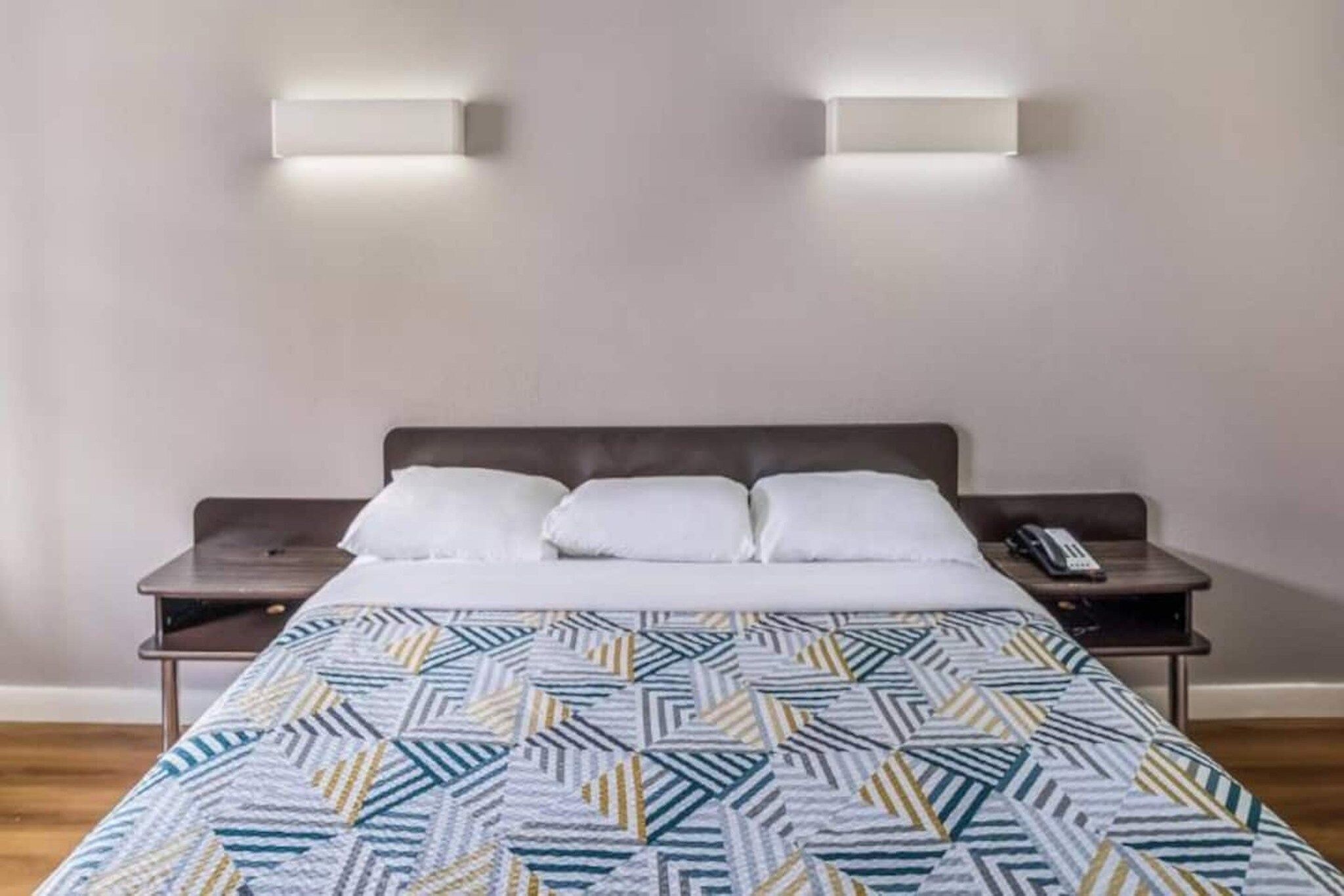 A hotel room with a bed, two bedside tables, and two wall-mounted lights.