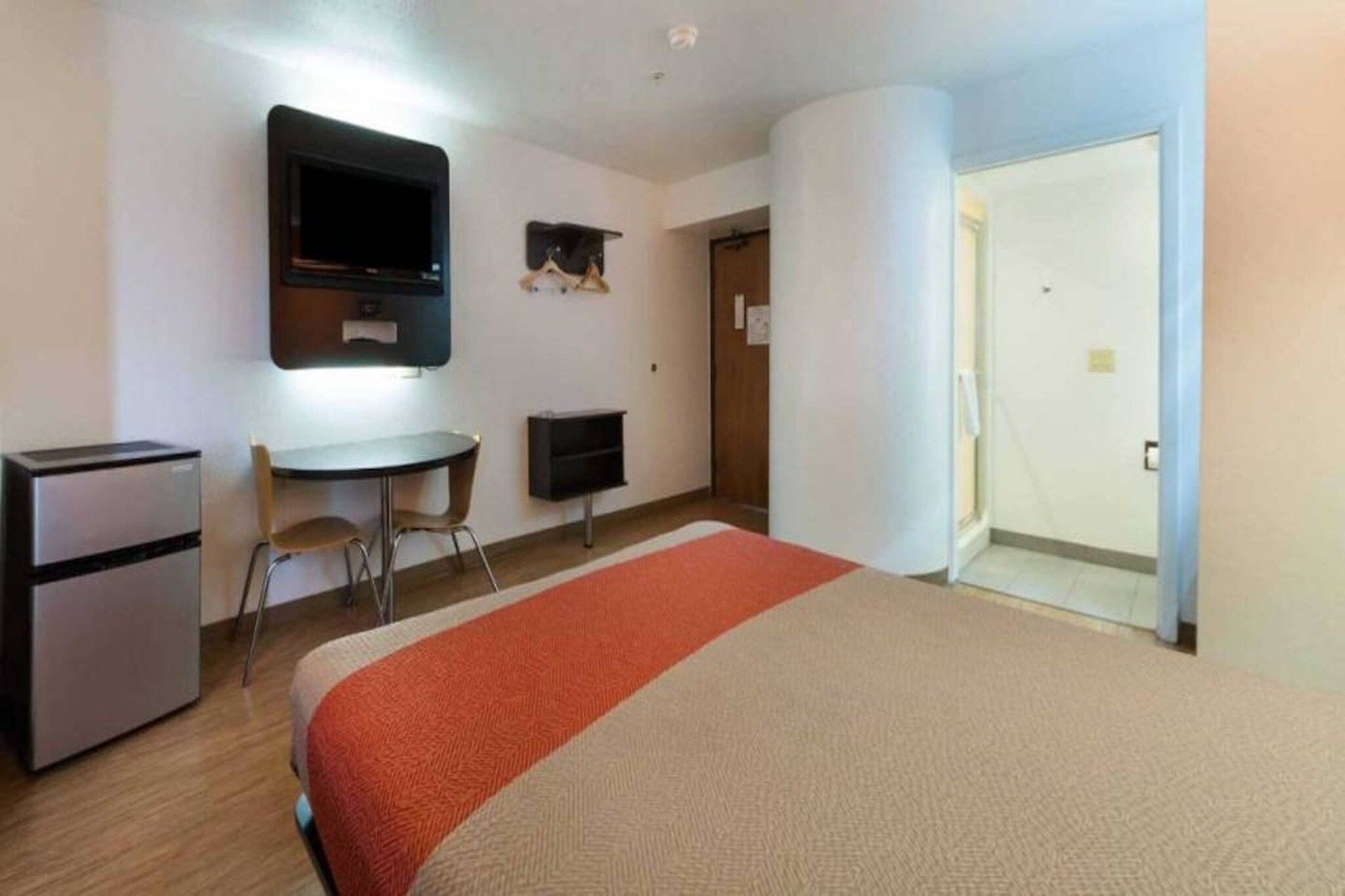 A hotel room with a bed, a desk, a television, and a refrigerator.