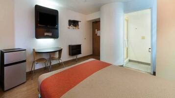 A hotel room with a bed, a desk, a television, and a refrigerator.