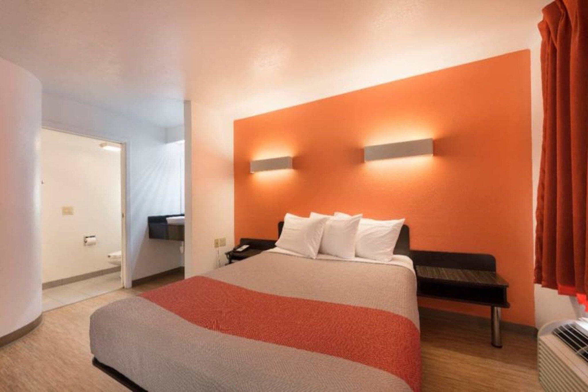 A hotel room with a bed, a bedside table, a nightstand, and a wall-mounted light fixture.