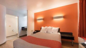 A hotel room with a bed, a bedside table, a nightstand, and a wall-mounted light fixture.