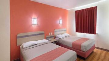 A hotel room with two beds, a wooden floor, and a red curtain.