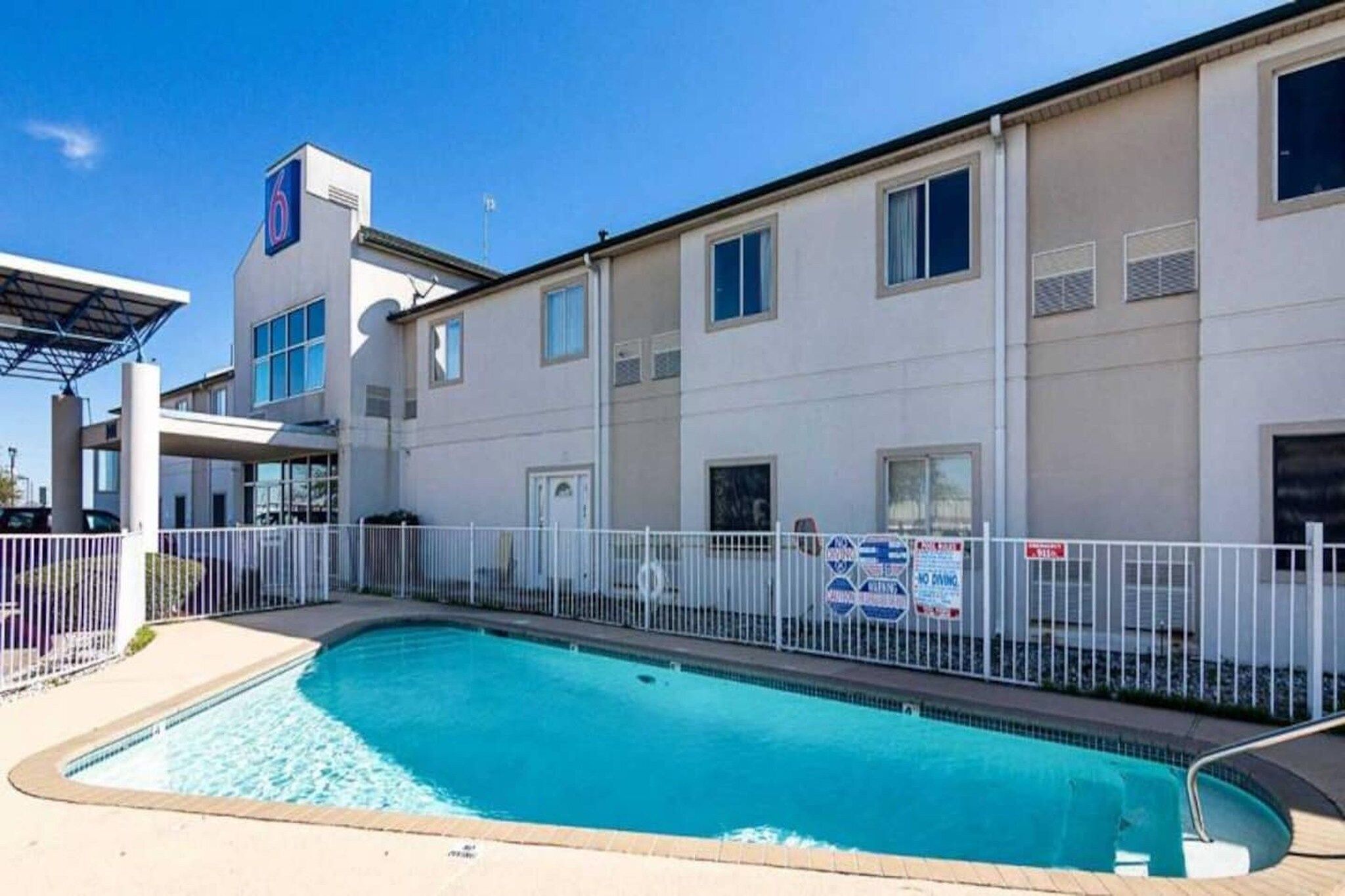 A swimming pool adjacent to a building with a white fence and a sign indicating no diving.
