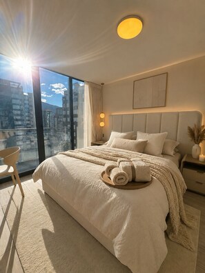 A hotel bedroom with a large bed, a nightstand, a chair, and a view of the city through a large window. - Beautiful view (Quito)