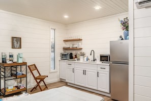 A kitchen with white cabinetry, a stainless steel refrigerator, a wooden chair, and a coffee station. - The Nest | Hocking Hills, Hot Tub, Pickleball (Creola)