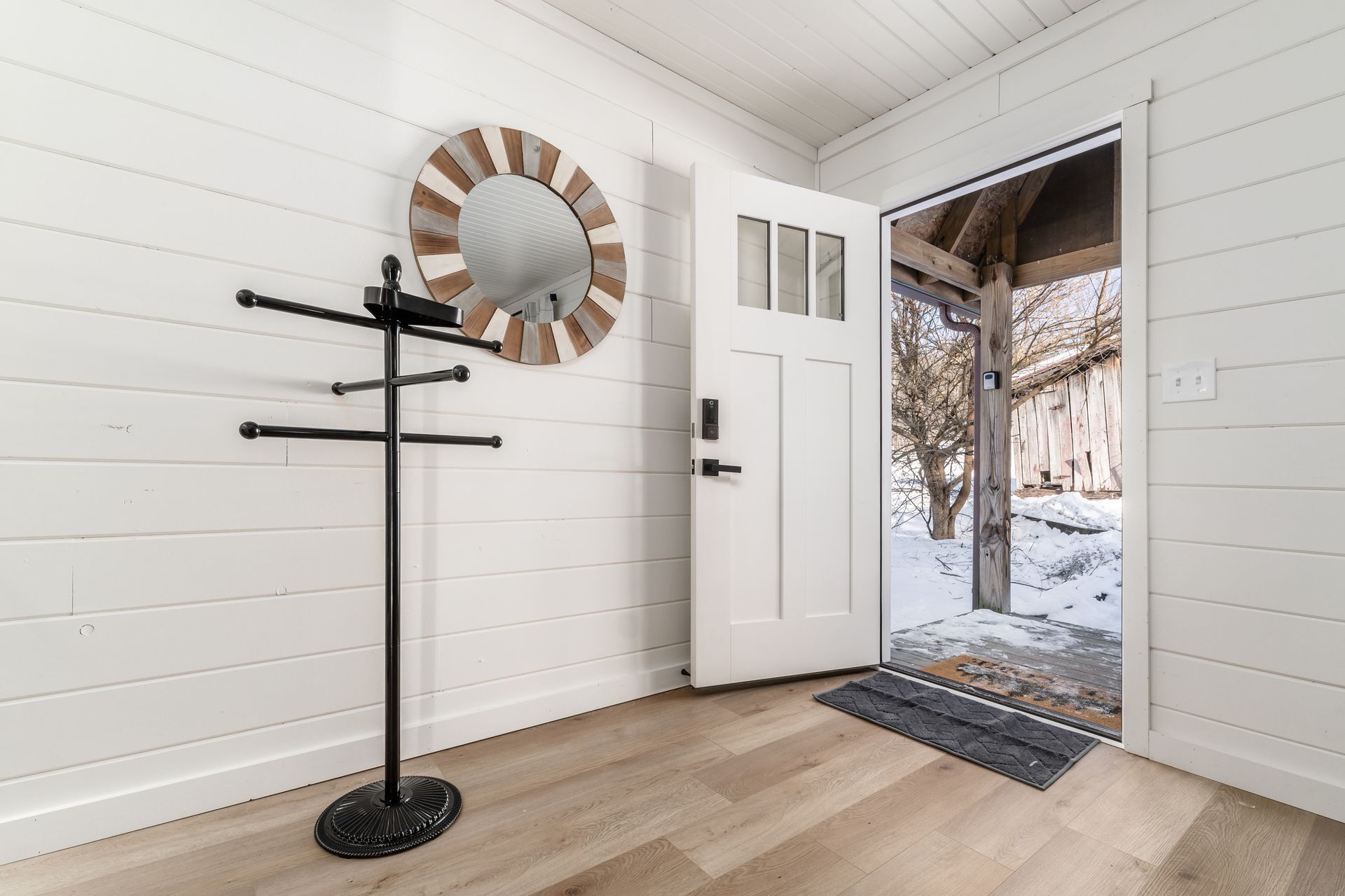 Un intérieur en bois peint en blanc, avec un porte-manteau, une porte et une vue sur un espace extérieur enneigé.