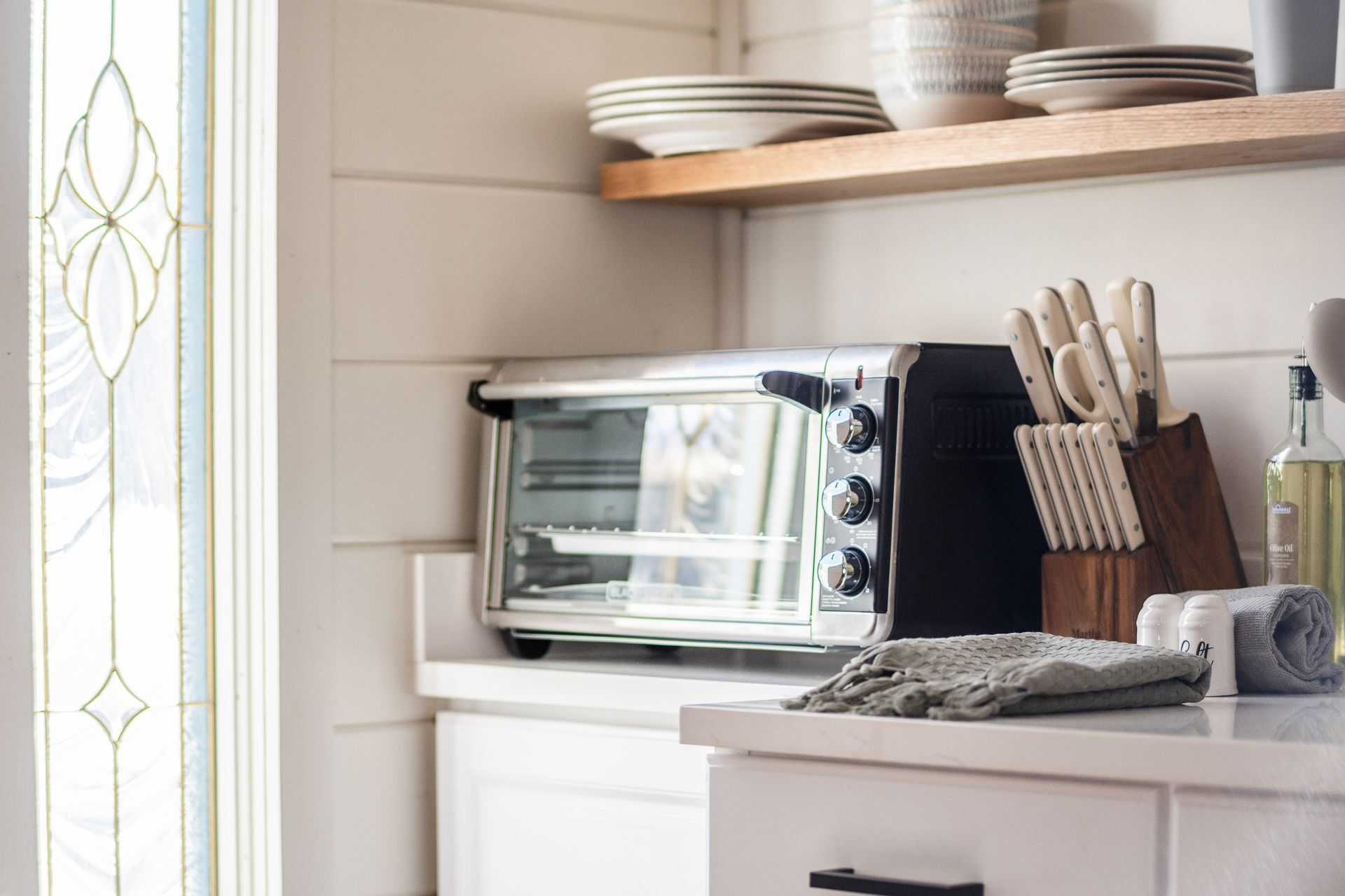 A kitchen with a toaster oven on the counter, a knife block, and a bottle of olive oil.
