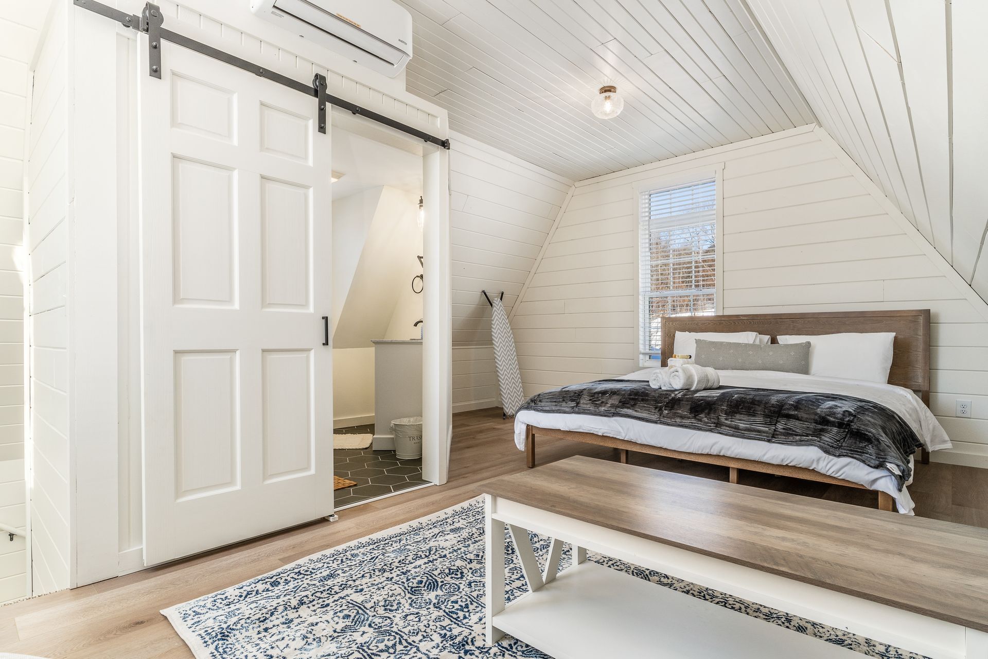 Een slaapkamer met een bed, een bankje, een schuifdeur, een raam en een airconditioning.