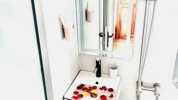 Ein Badezimmer mit einem weißen Waschbecken, einem Spiegel, einer Dusche und einem gemusterten Boden.