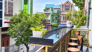 A balcony with a glass barrier, a small tree, and a seating area with stools.