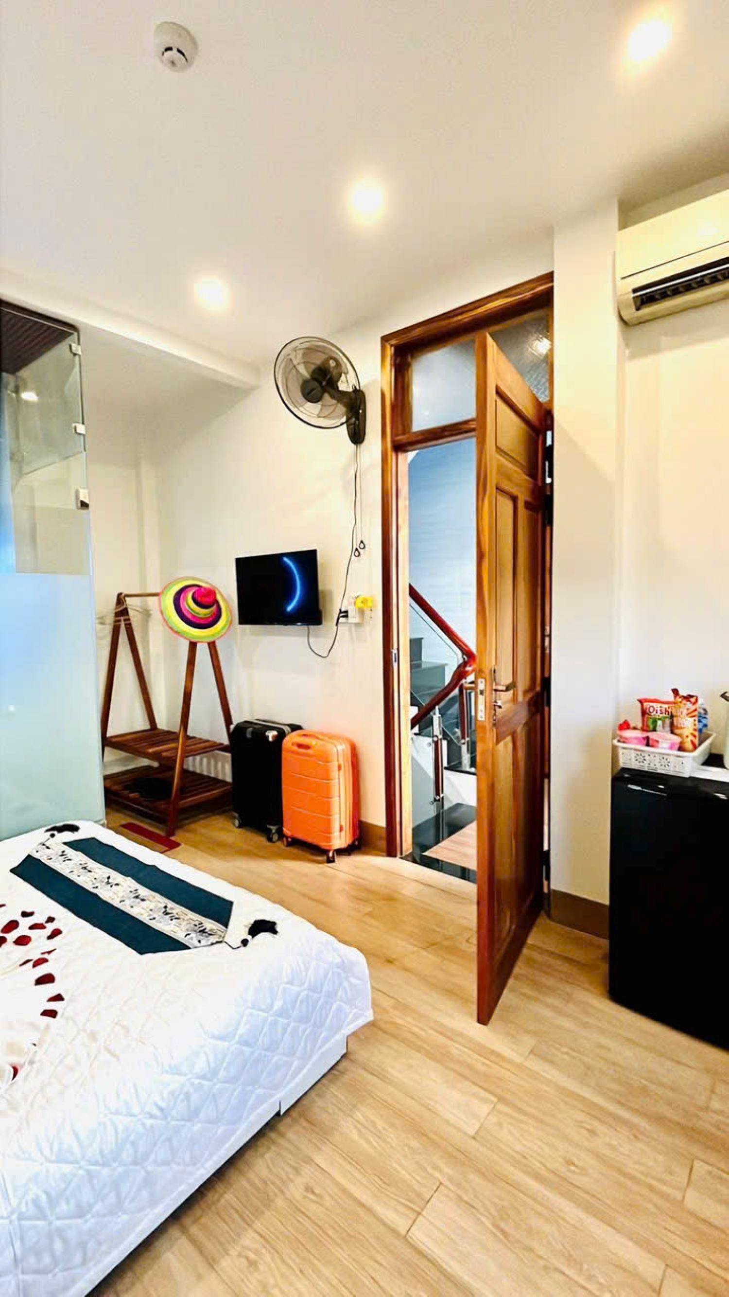 Ein Schlafzimmer mit einem Bett, einem Koffer, einem Fernseher, einem Ventilator und einer Tür zu einer Treppe.