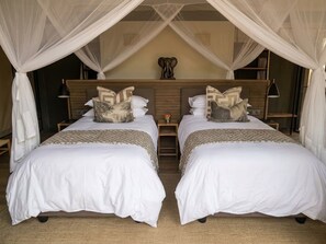 Cama de casal com dossel, mesa de cabeceira e cabeça de elefante decorativa.