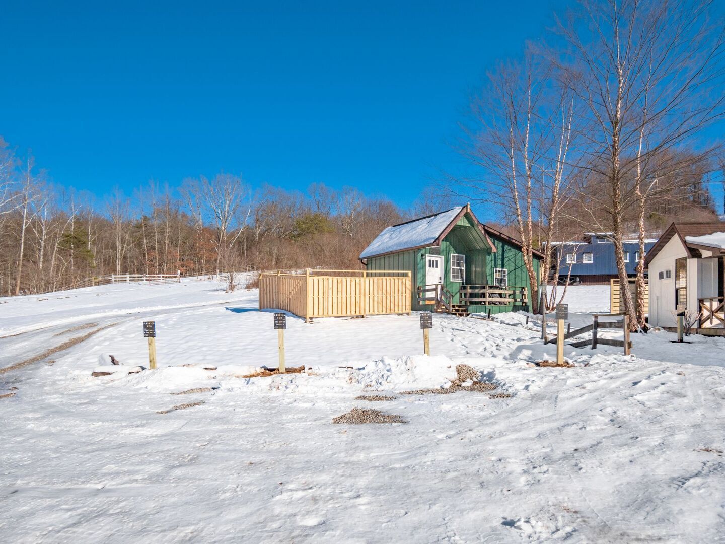 A snow-covered landscape with a green building, a wooden fence, and a clear blue sky.