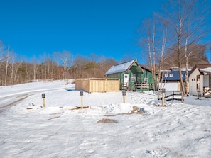 A snow-covered landscape with a green building, a wooden fence, and a clear blue sky. - Scouts Cottage | Hocking, Pickleball, Hot Tub (Creola)