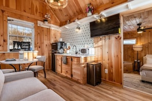 A cozy cabin interior with a wooden interior, a kitchenette, a seating area, and a television mounted on the wall. - Scouts Cottage | Hocking, Pickleball, Hot Tub (Creola)